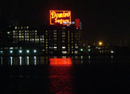 Night image of huge iconic red neon Domino Sugars sign, 120 feet by 70 feet, reflecting on the Patapsco River since 1951, taken from Harbor East looking at Locust Point, Baltimore, MD