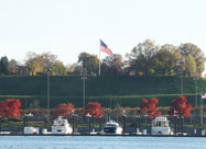 Image of Federal Hill Park in November viewed fron across the harbor with U.S. flags flying, colorful fall foliage & yachts in the foreground, Baltimore, MD